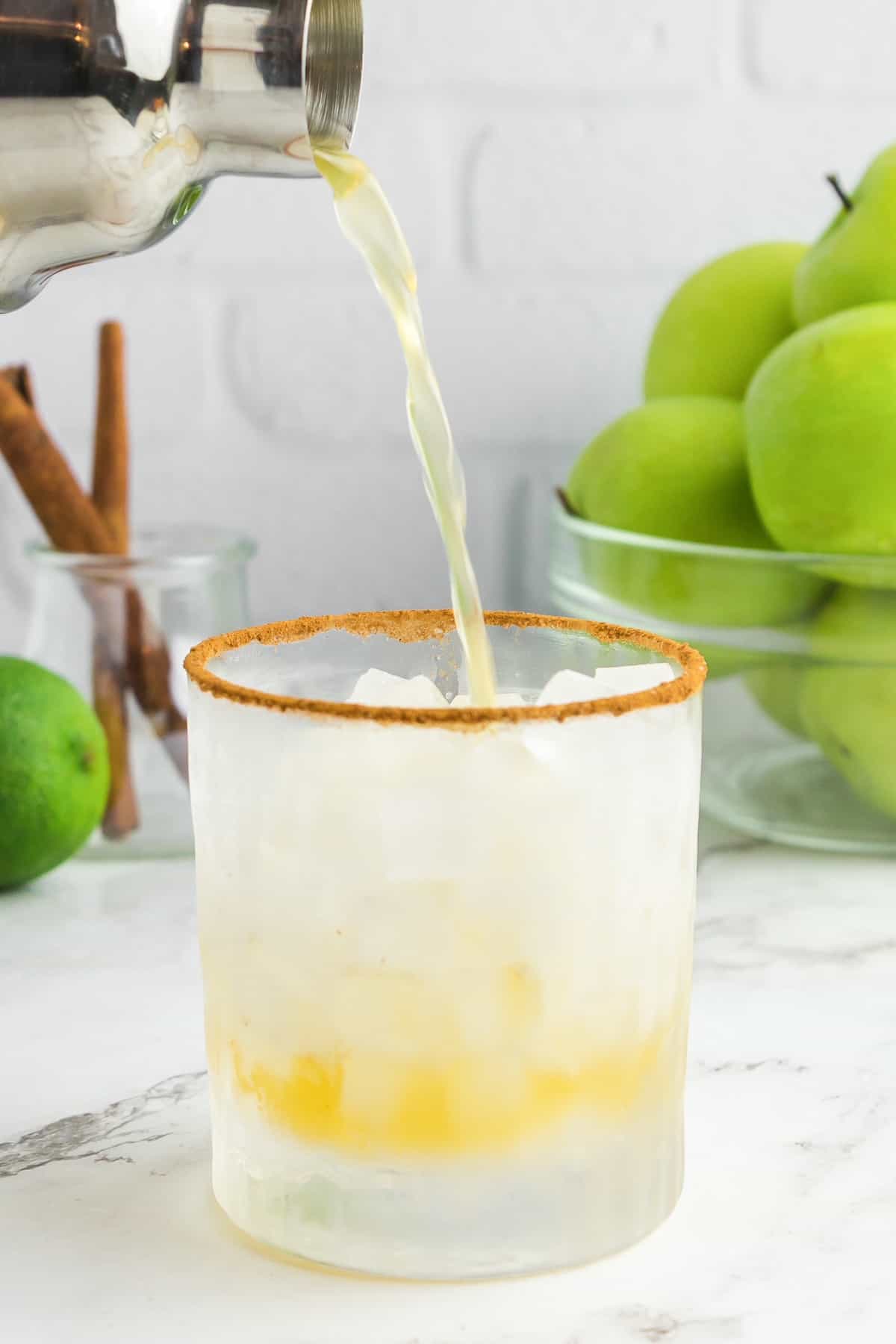 Apple cider margarita being poured into a glass with ice.