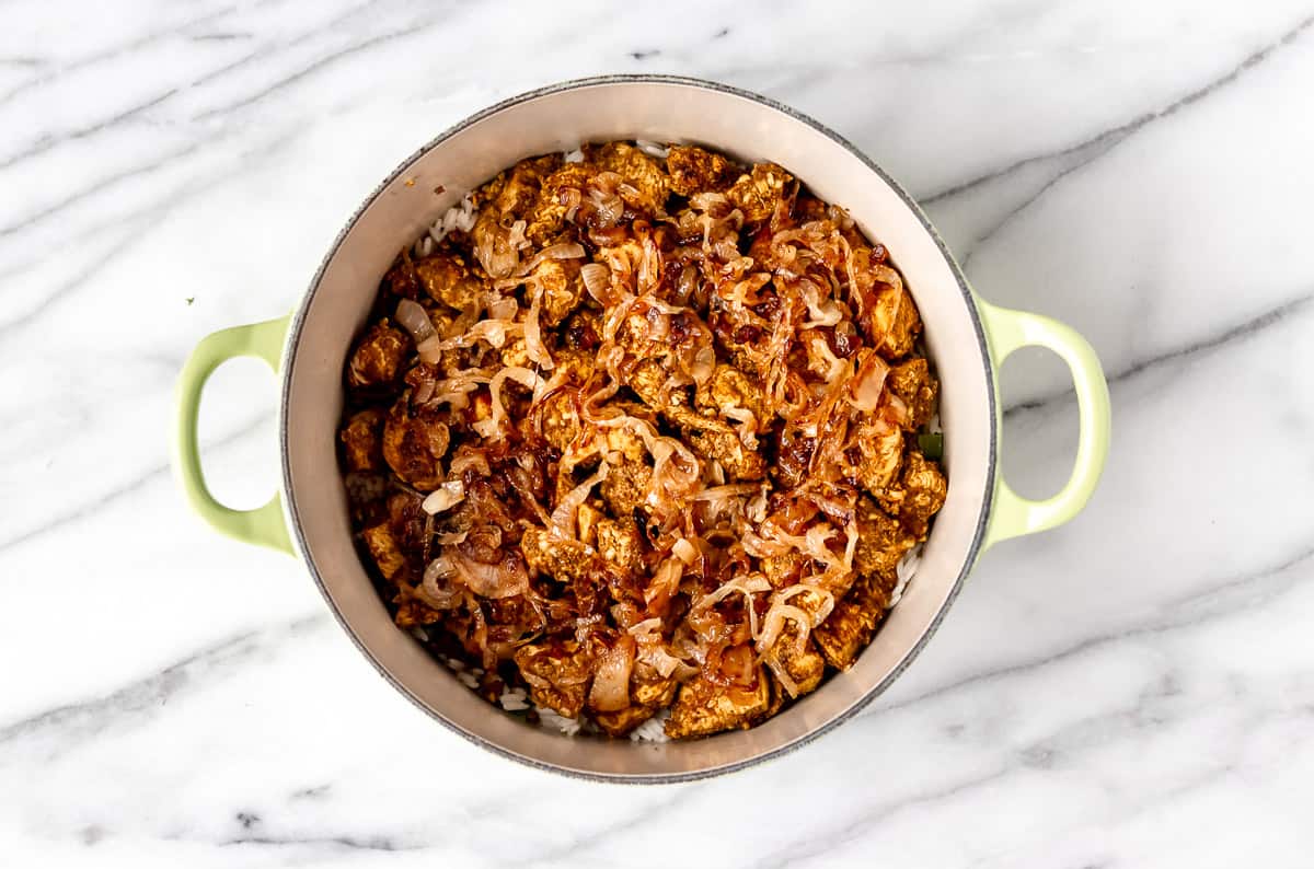 A layer of rice topped with chicken and caramelized onions in a Dutch oven.