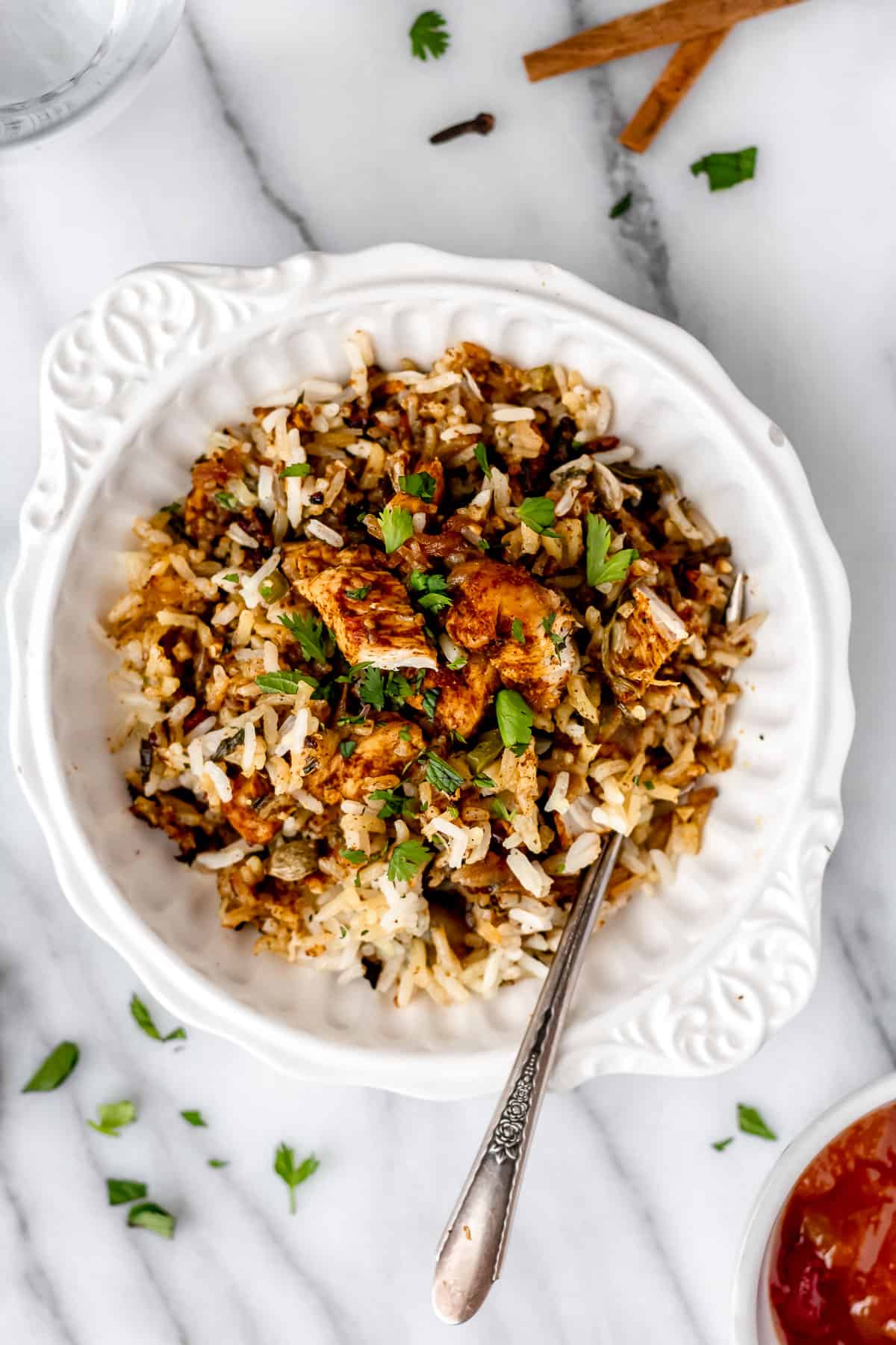 Overhead of chicken biryani in a white bowl with spices around it.