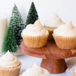 Eggnog cupcakes on a wood stand and in front of it with faux mini christmas trees in the background.