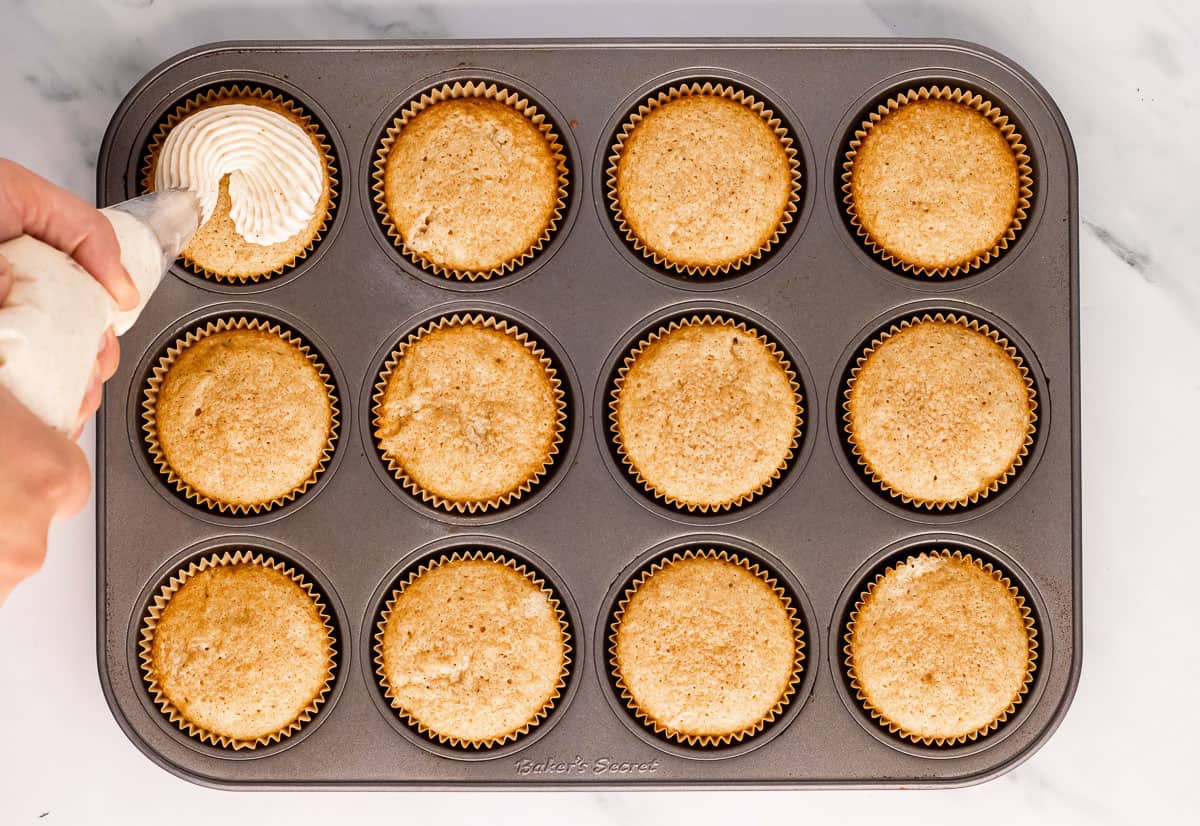 Frosting being piped onto a cupcake in a cupcake pan.