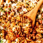 Close up of a wood spoon in a ground beef pasta skillet with text overlay.
