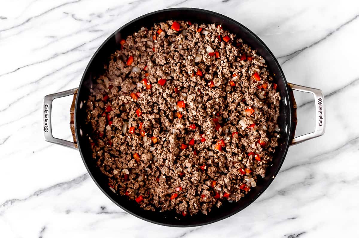 Ground beef, pepper, onion and garlic cooking in a black skillet.