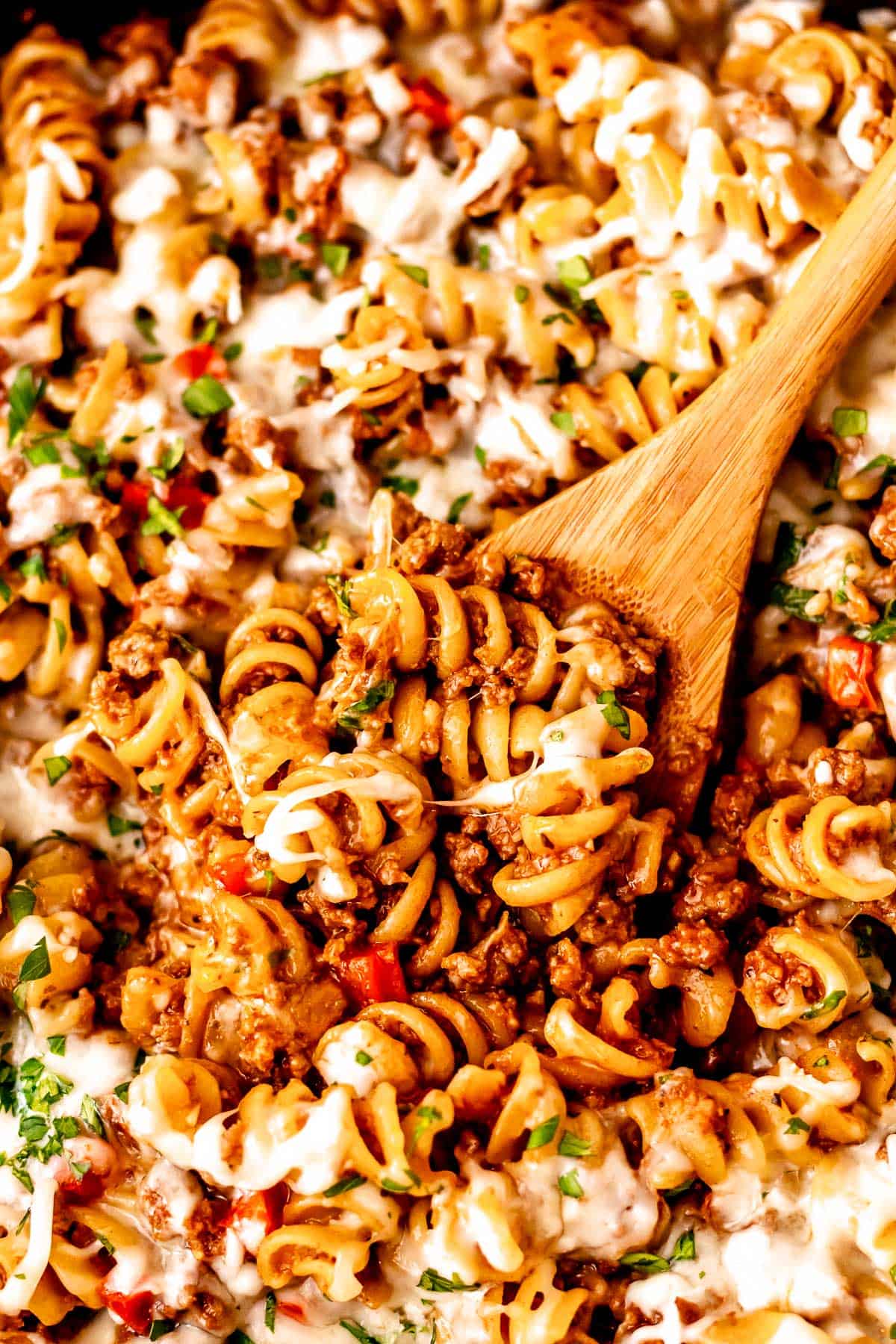 Close up of a wood spoon in a ground beef pasta skillet.