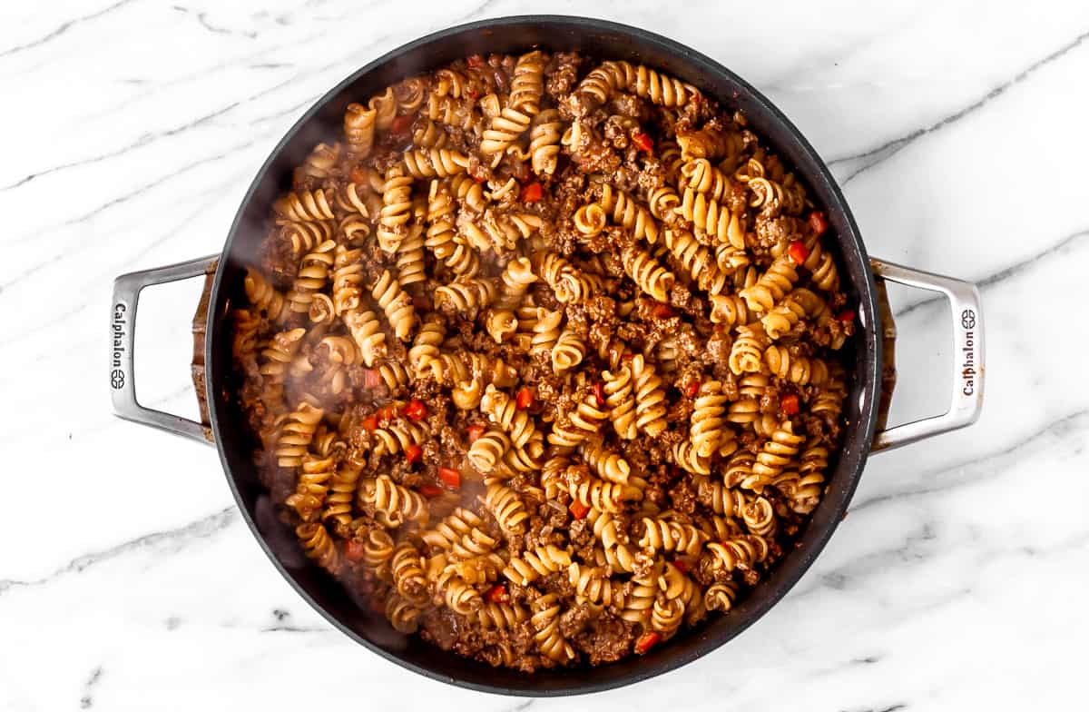 Ground beef and pasta in a black skillet.