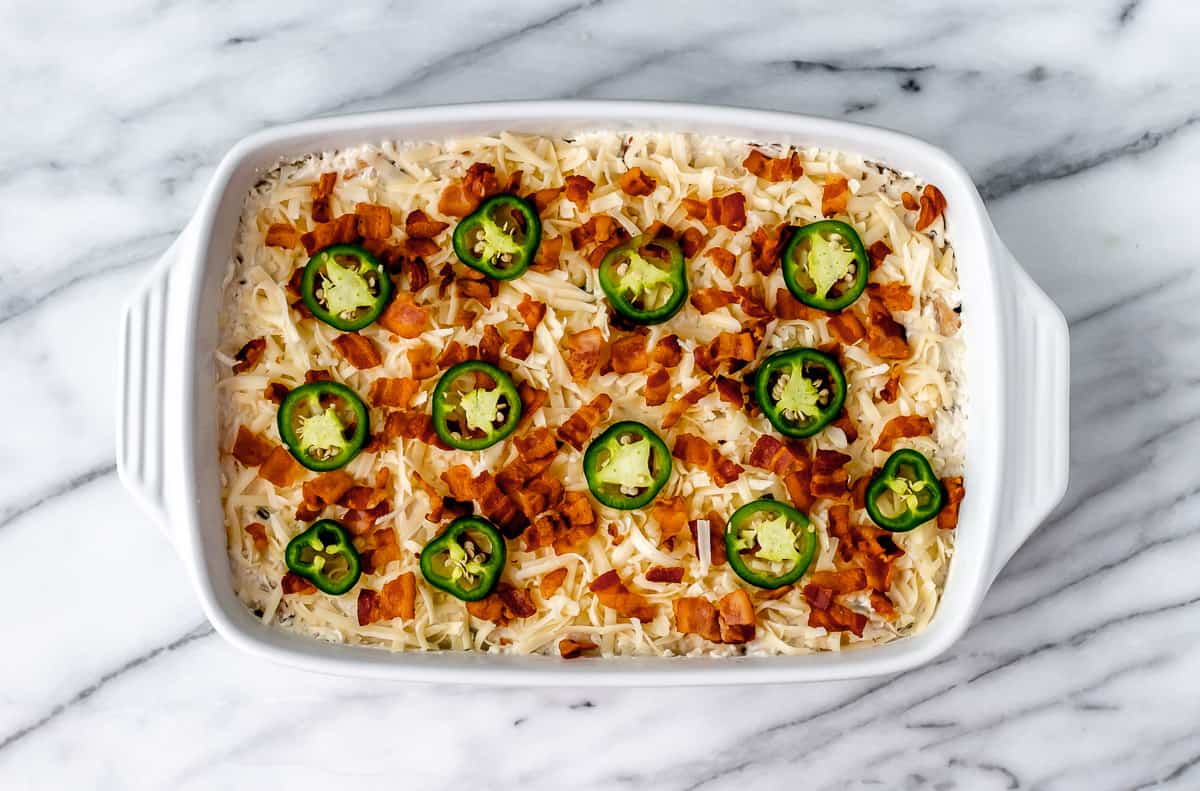 A jalapeno popper chicken casserole topped with slices of jalapeno peppers and bacon.