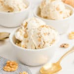 Maple walnut ice cream in three white bowls with a gold spoon and walnuts around them.