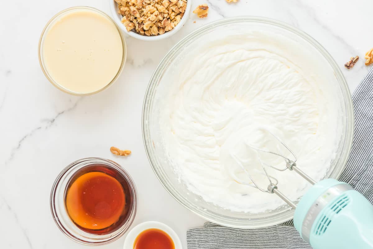 Whipped cream in a mixing bowl with other ingredients around it.