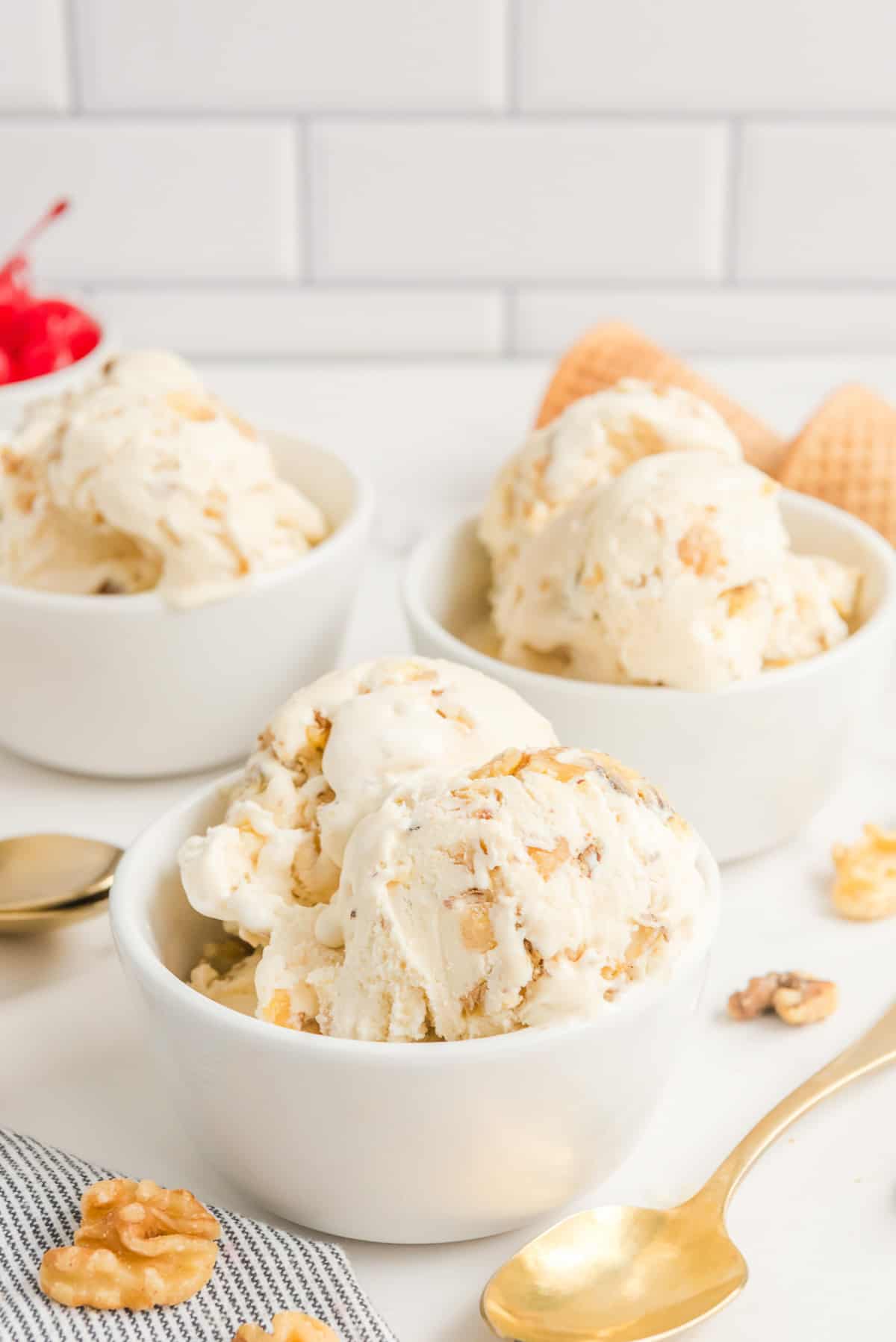 Maple walnut ice cream in three white bowls with a gold spoon and walnuts around them.