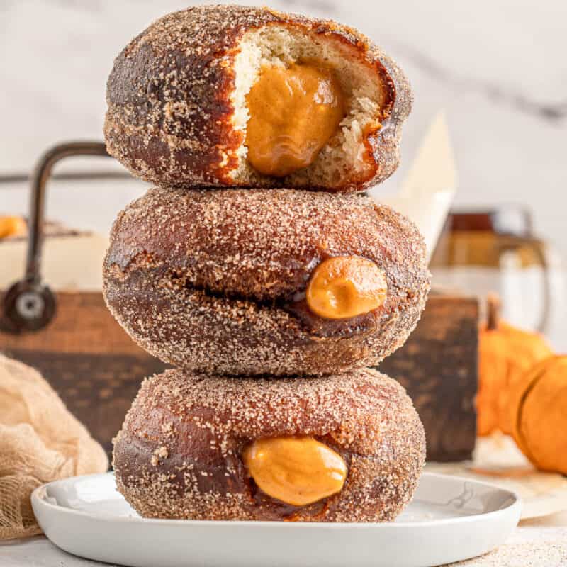 Three pumpkin filled donuts stacked on top of each other with a bite taken out of the top one.