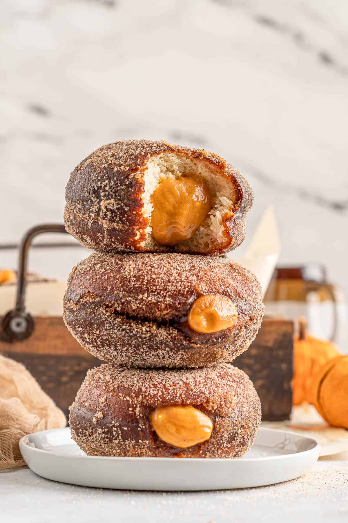 Three pumpkin filled donuts stacked on top of each other with a bite taken out of the top one.