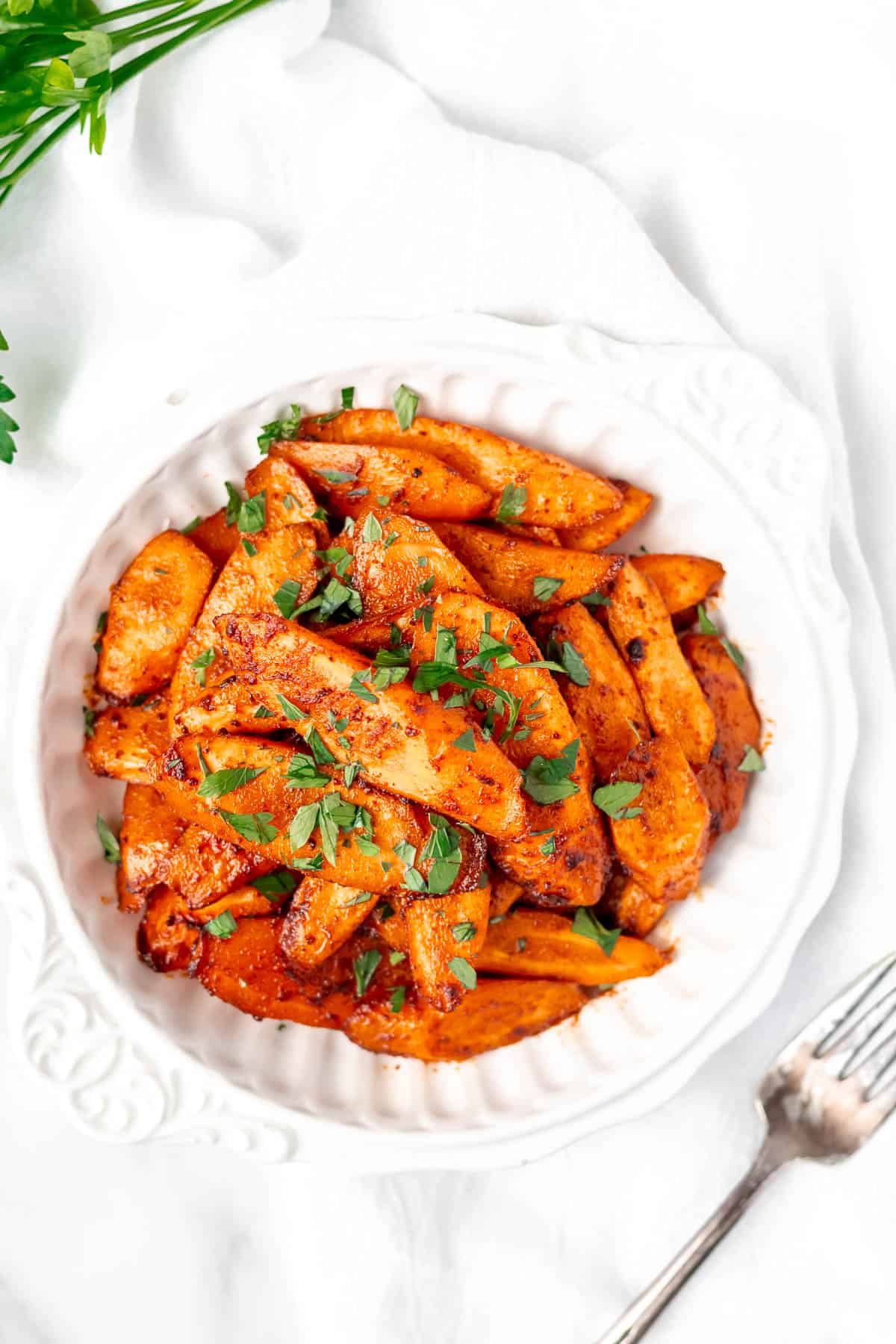 Overhead view of a bowl of roasted spiced carrots with a fork and cilantro around it.