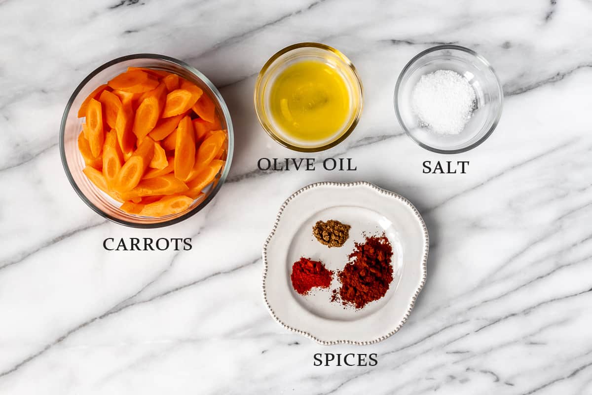 Ingredients to make spiced roasted carrots on a marble background with text overlay.