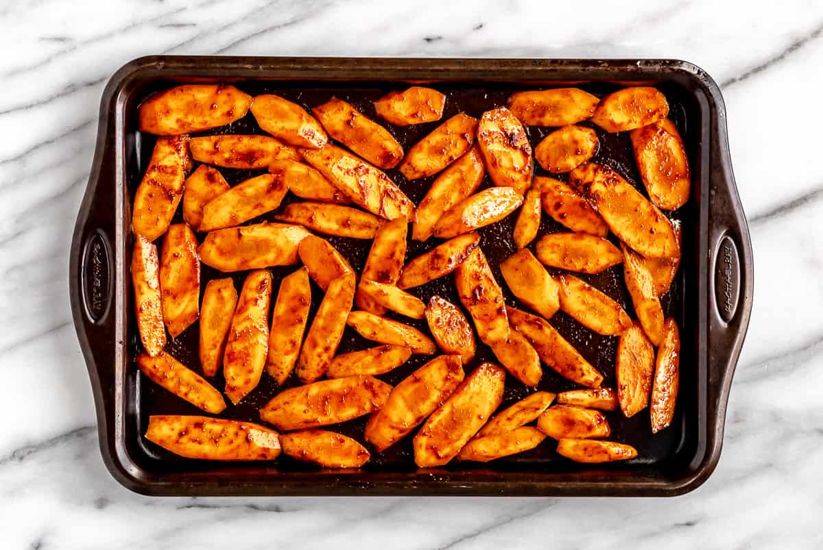 Slices of carrots with seasoning on a baking sheet.