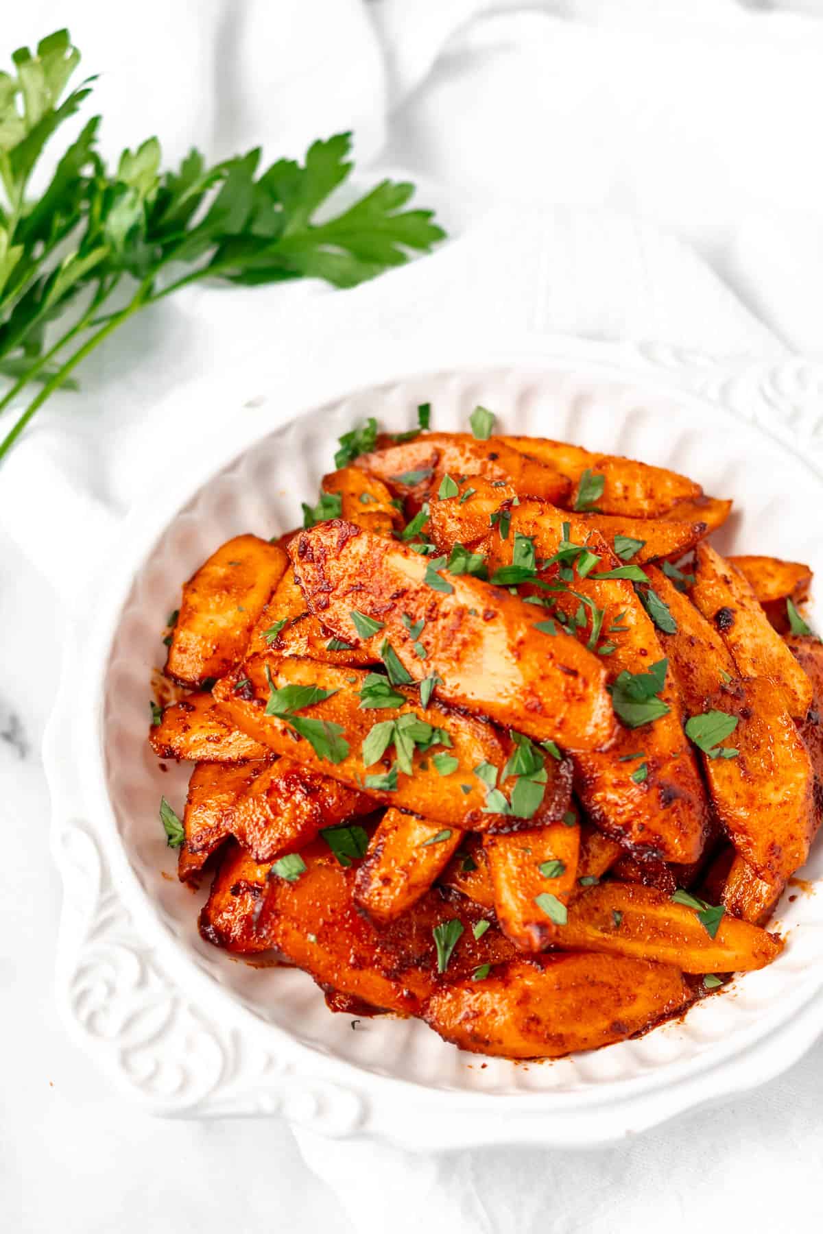 A bowl of spiced roasted carrots with cilantro in the background.