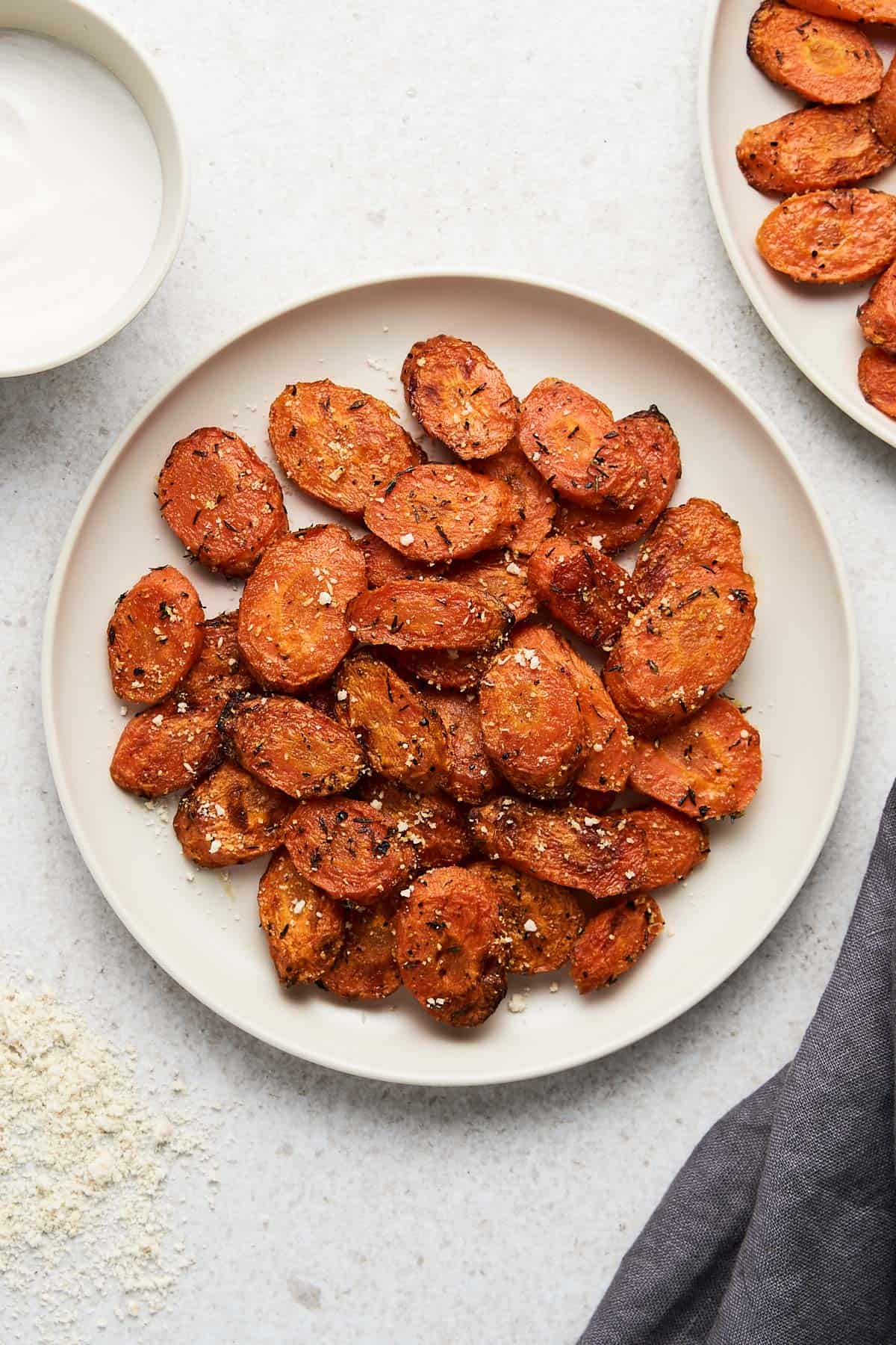 Overhead of a cream colored plated with air fried carrots on it, a second plate partially showing in the background and a gray kitchen towel on the side.