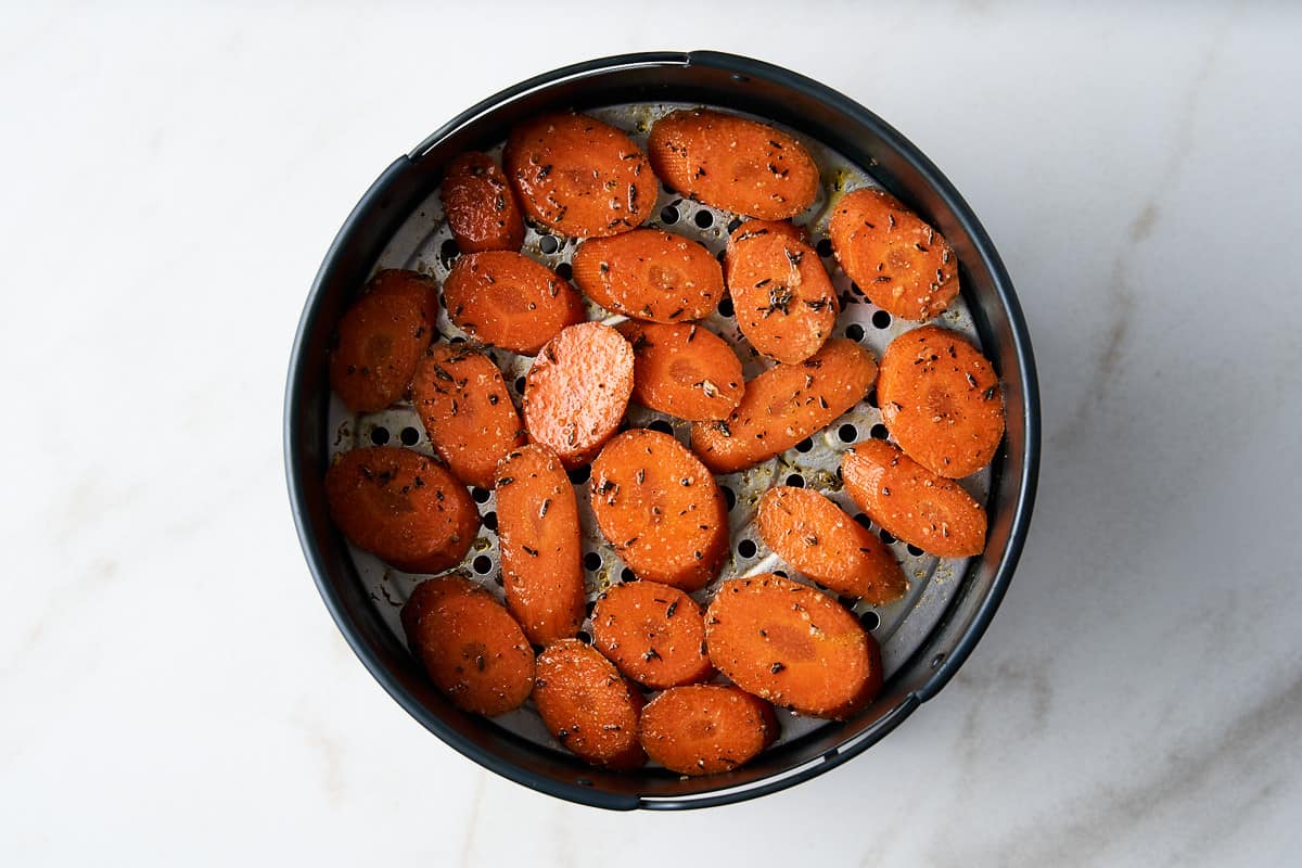 Raw, seasoned carrot slices in an air fryer basket.