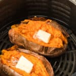 Two sweet potato halves topped with butter in an air fryer.