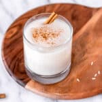 A glass of almond milk horchata on a wood server over a white backdrop.