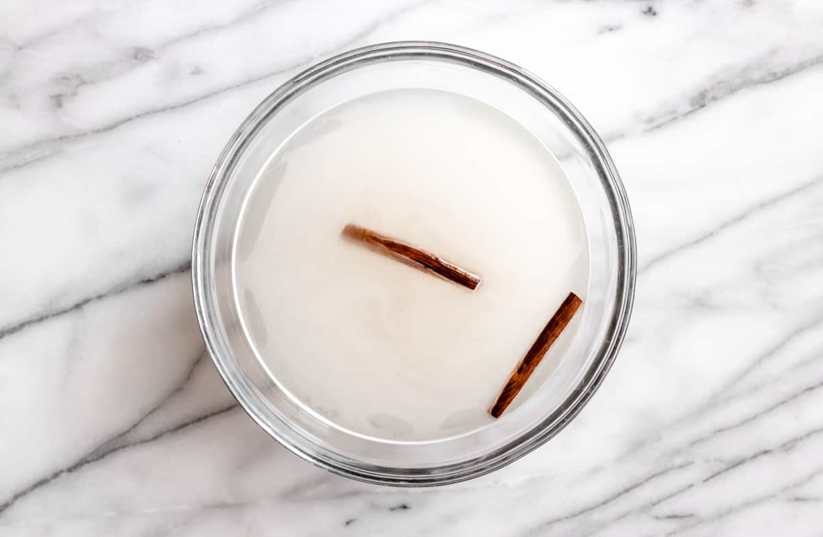 Rice, water and cinnamon sticks in a glass bowl over a marble background.