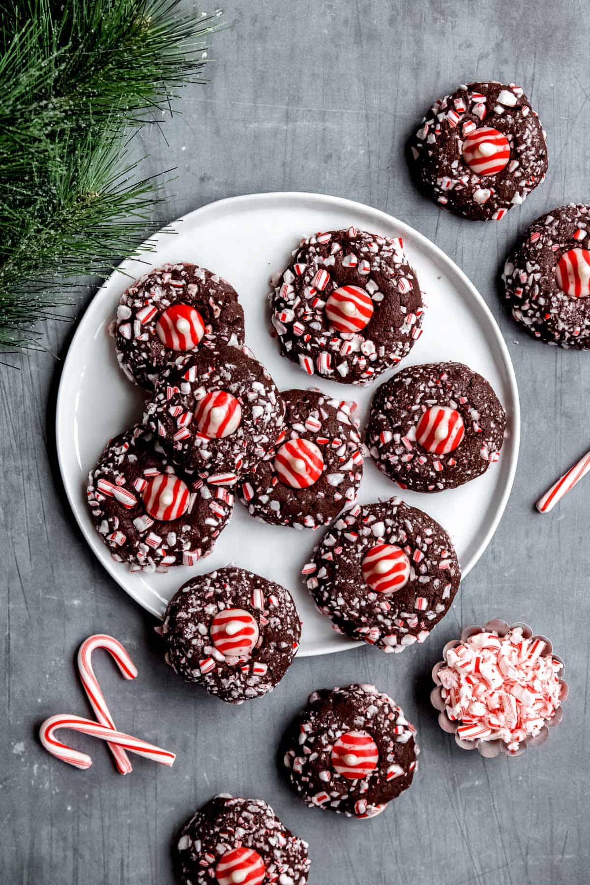 A plate of chocolate peppermint kiss cookies with extra cookies and candy canes around it.