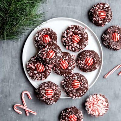 A plate of chocolate peppermint kiss cookies with extra cookies and candy canes around it.