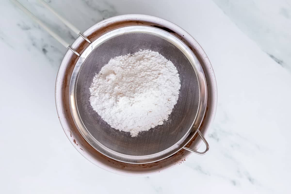Flour in a sifter over a bowl of batter.