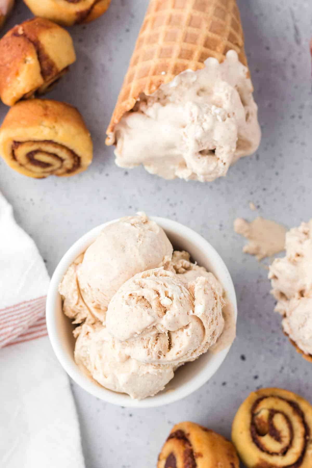 Cinnamon ice cream in a bowl with cones of ice cream and cinnamon rolls around it.