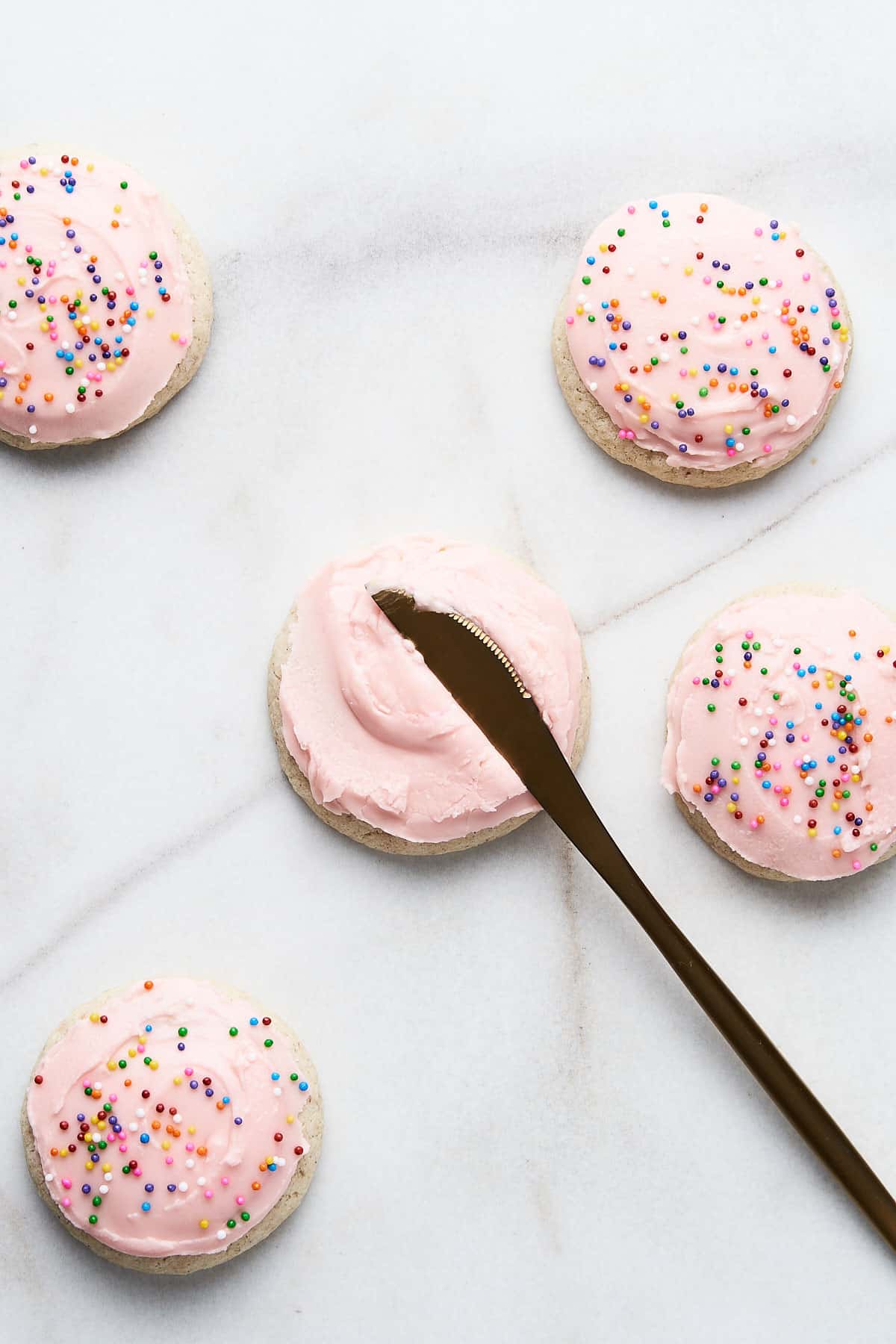 Sugar cookies being frosting with a butterknife and decorated with sprinkles.