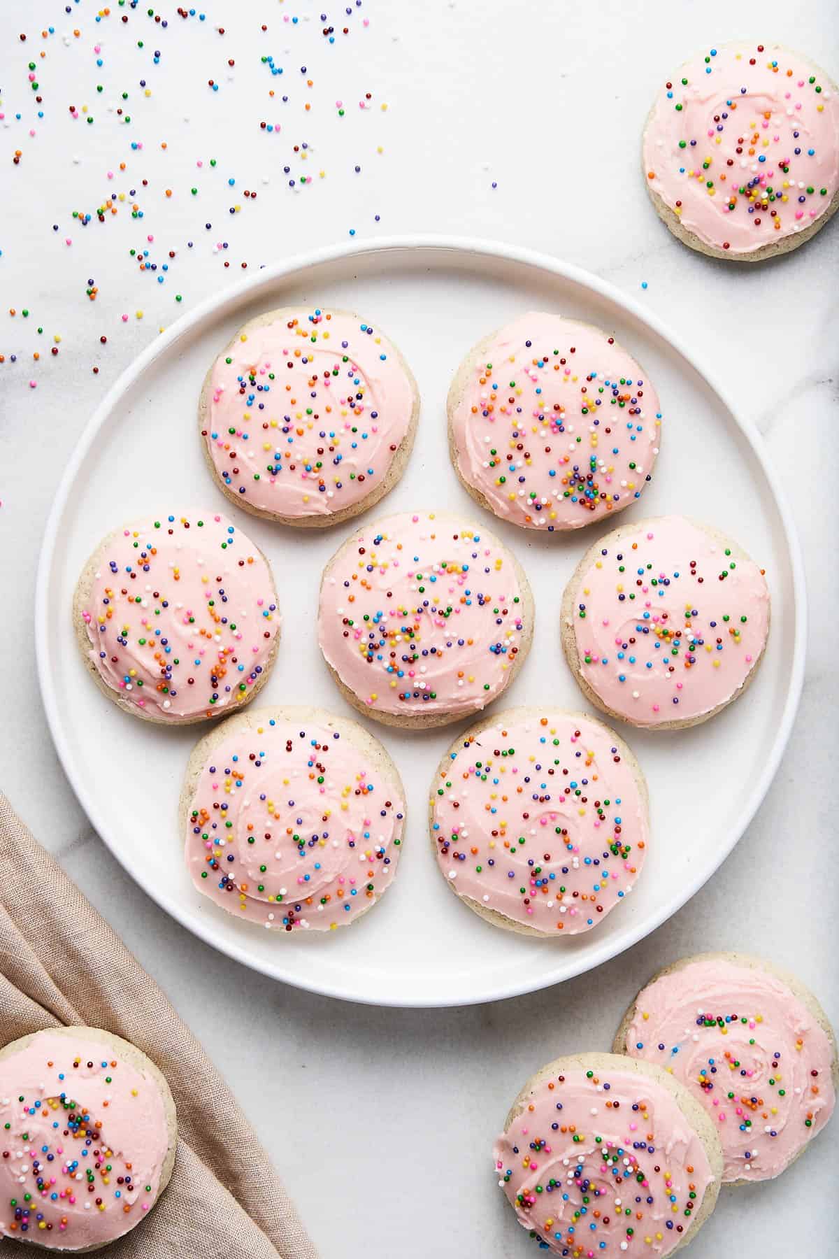 Gluten free sugar cookies on a white plate with more cookies and sprinkles around the plate.