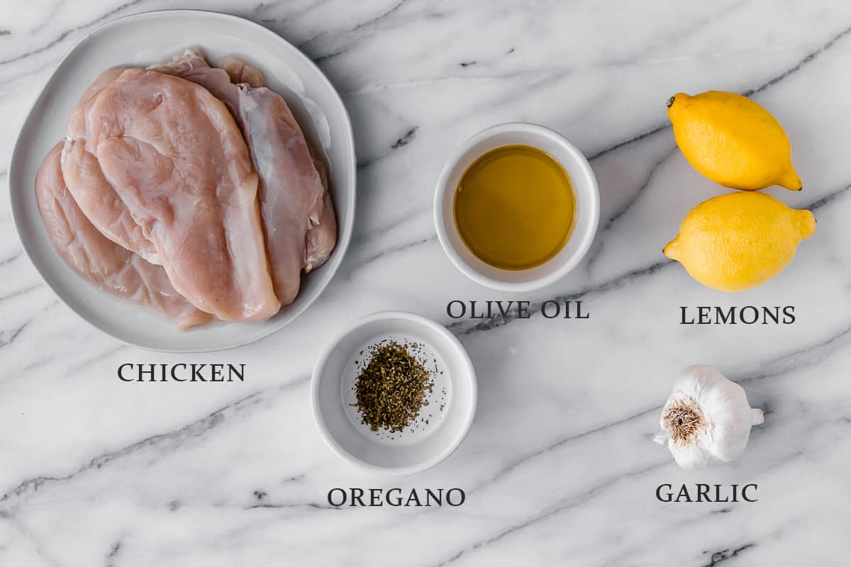 Ingredients needed to make Greek chicken on a marble background with text overlay.