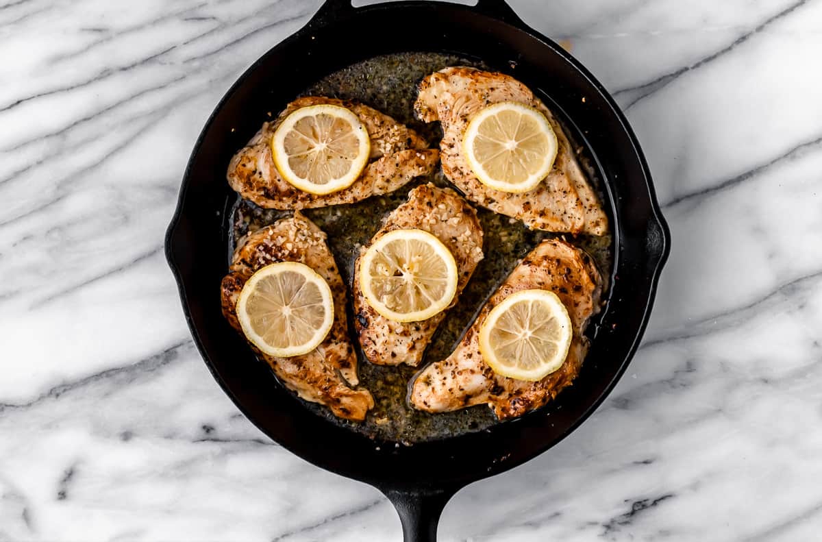 Seared chicken breasts with lemon slices on top in a cast iron skillet.