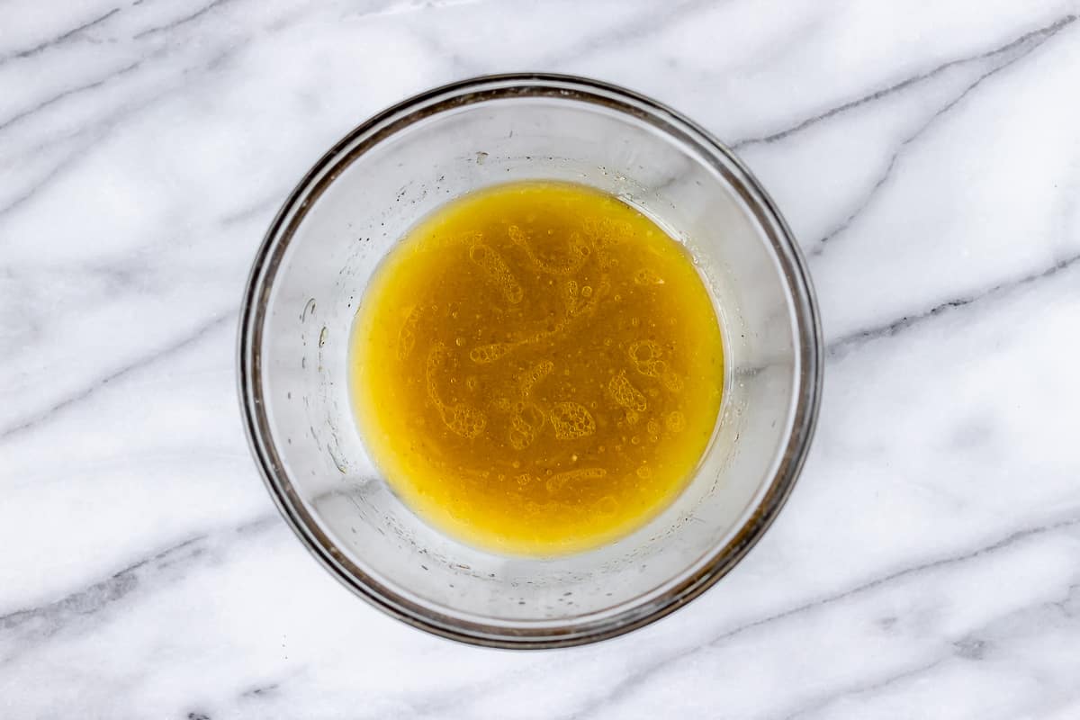 Marinade for Greek roasted potatoes in a glass bowl on a marble background.