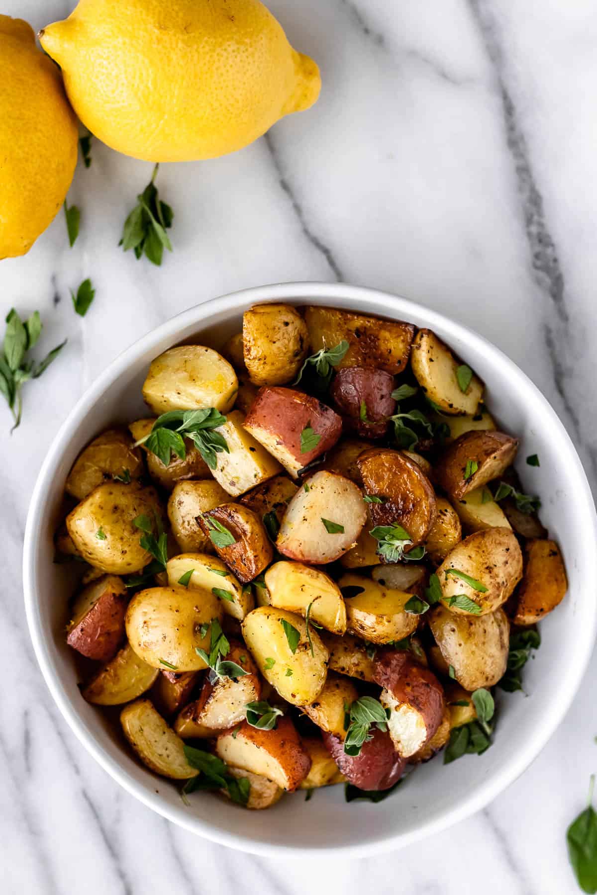 Overhead of Greek roasted potatoes with lemons and oregano leaves around it.