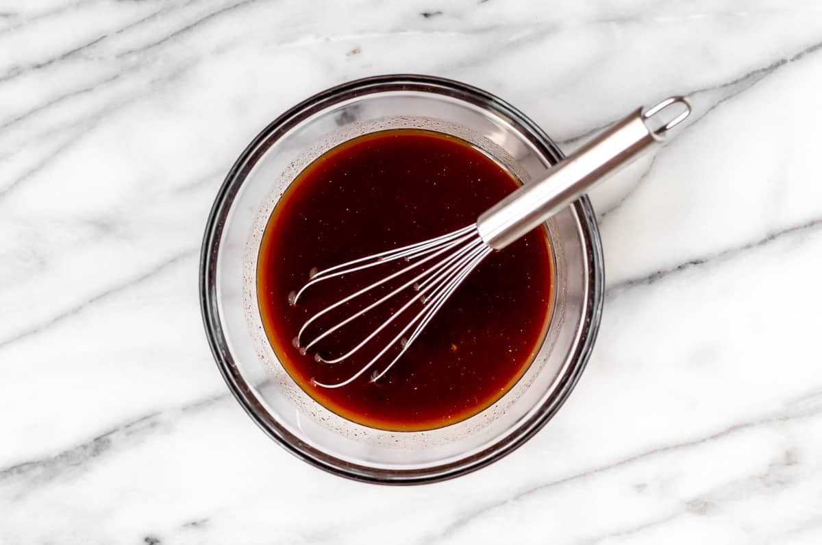 Brown sauce in a clear bowl with a whisk.