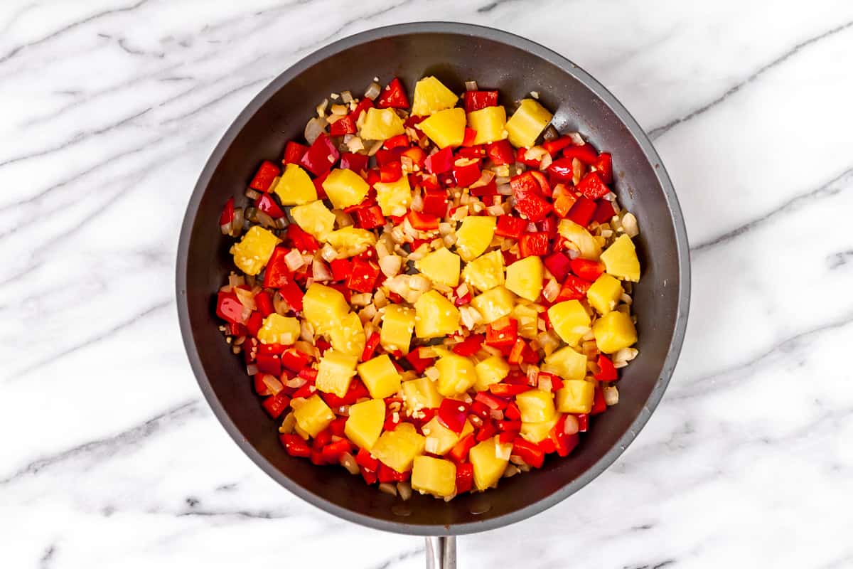 Peppers, onion, pineapple and garlic in a skillet.