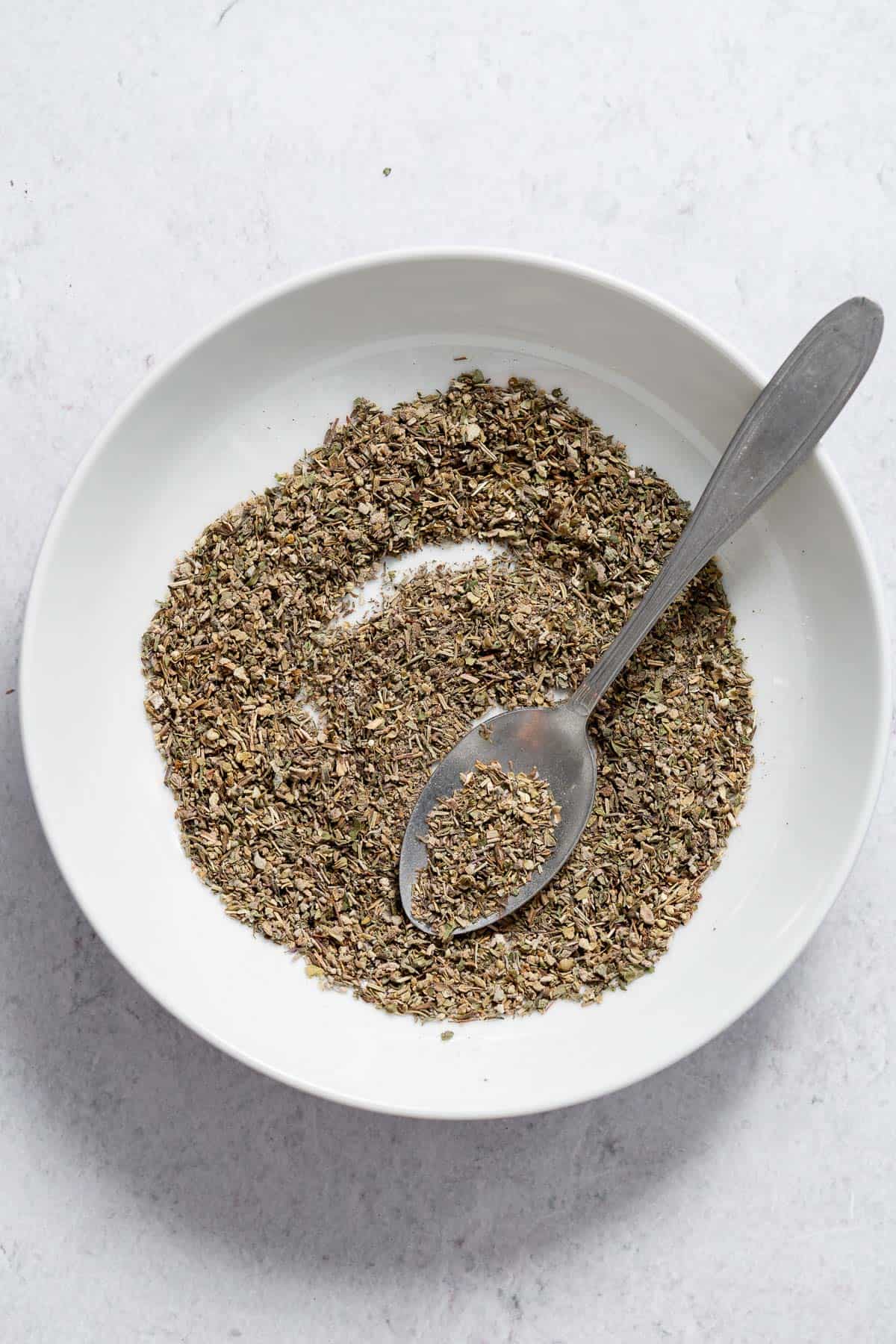 Overhead of poultry seasoning in a white bowl with a spoon.
