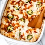 A jalapeno popper chicken casserole with a wood server lifting some up.