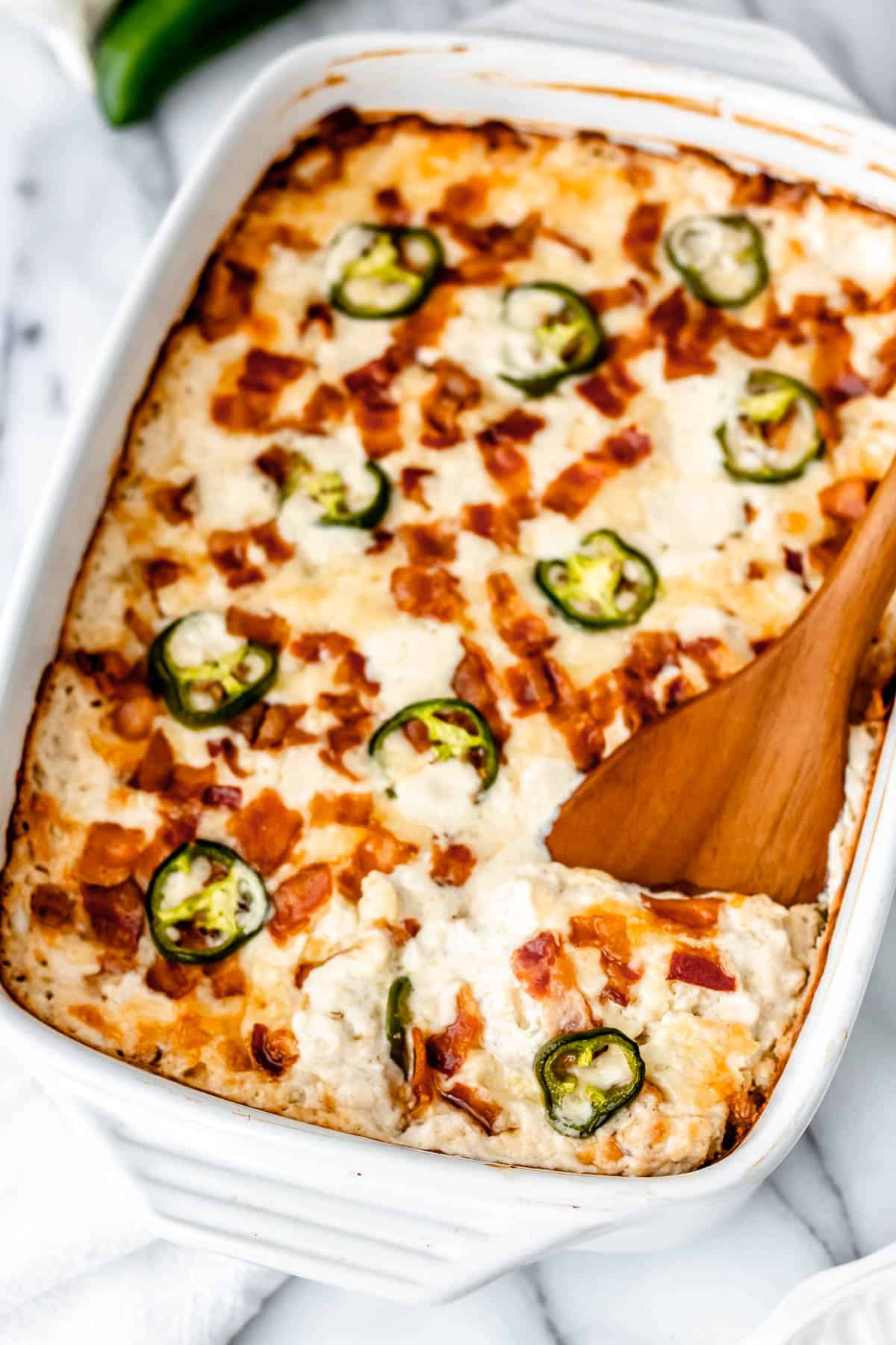 A jalapeno popper chicken casserole with a wood server lifting some up.