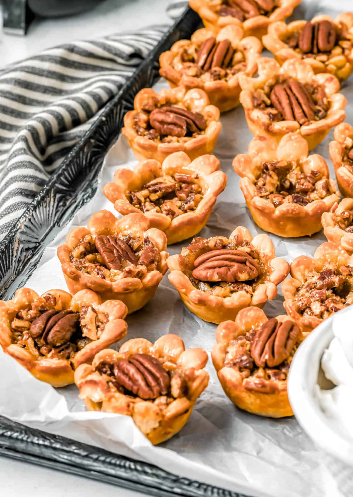 Close up of mini pecan pies on a parchment paper lined baking sheet with a striped towel in the background.