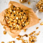 Pumpkin Spice Caramel Popcorn in a parchment paper lined container with popcorn around it.