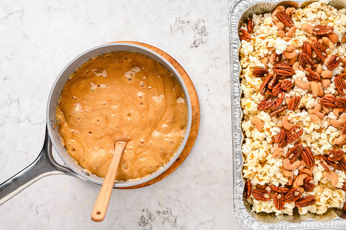 Caramel sauce in a sauce pan next to a tray of popcorn and nuts.