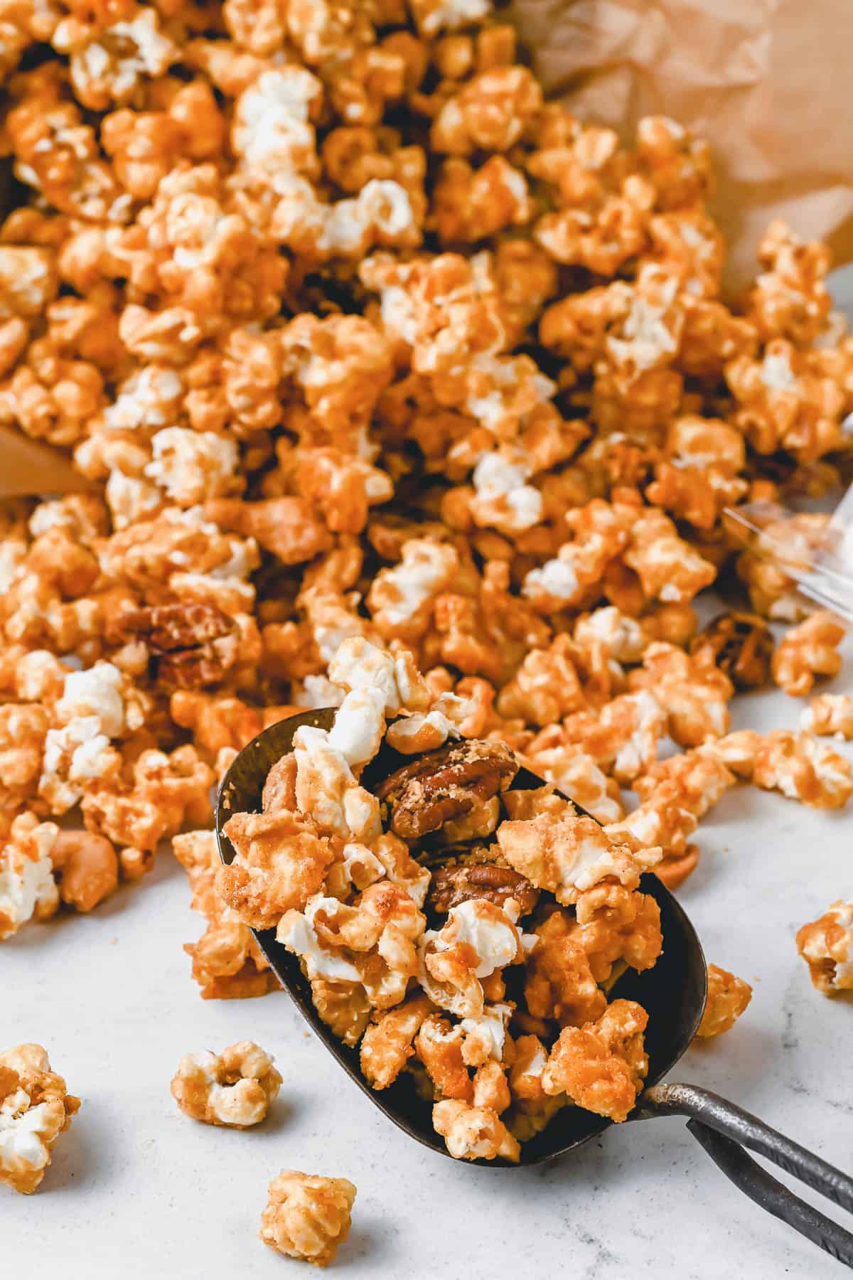 A scoop full of pumpkin spice caramel popcorn with a lot more around it.