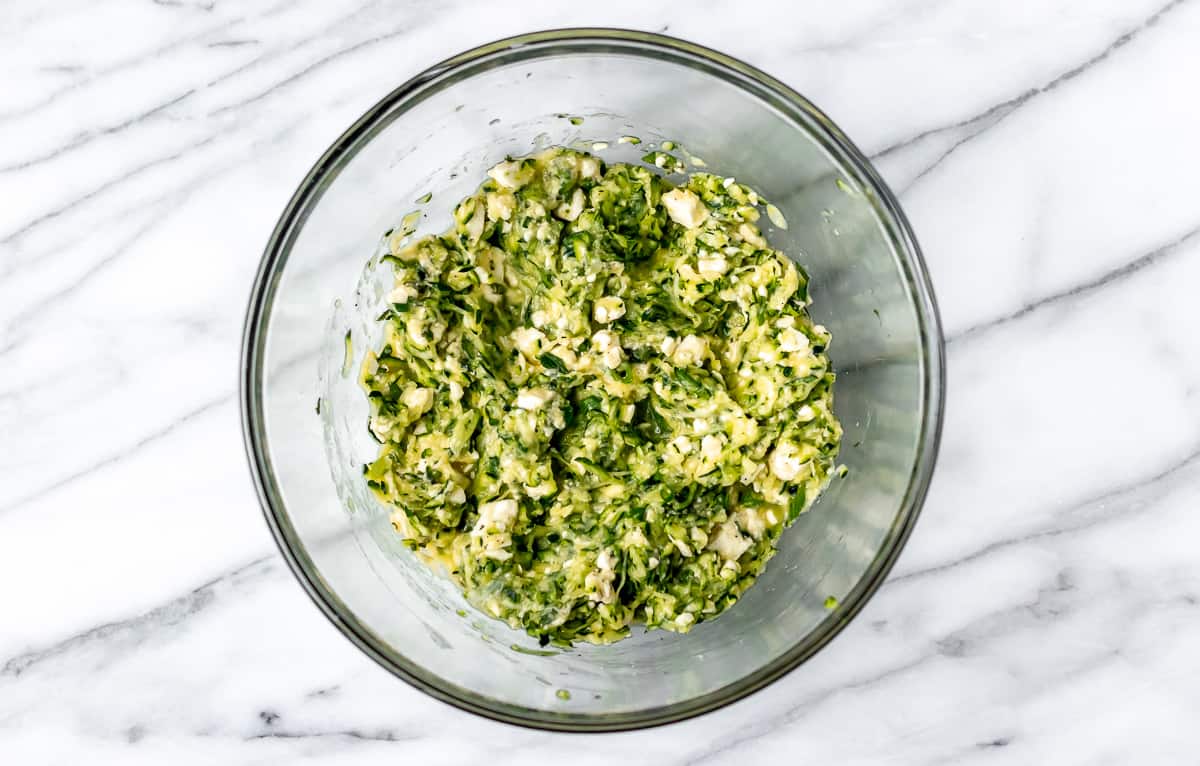 Zucchini, feta and herbs combined in a glass bowl.
