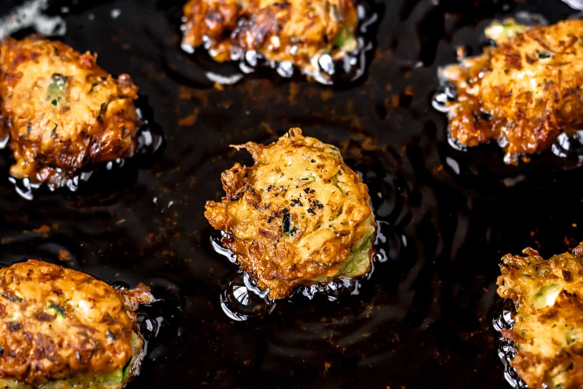 Close up of zucchini balls frying in oil in a cast iron skillet.