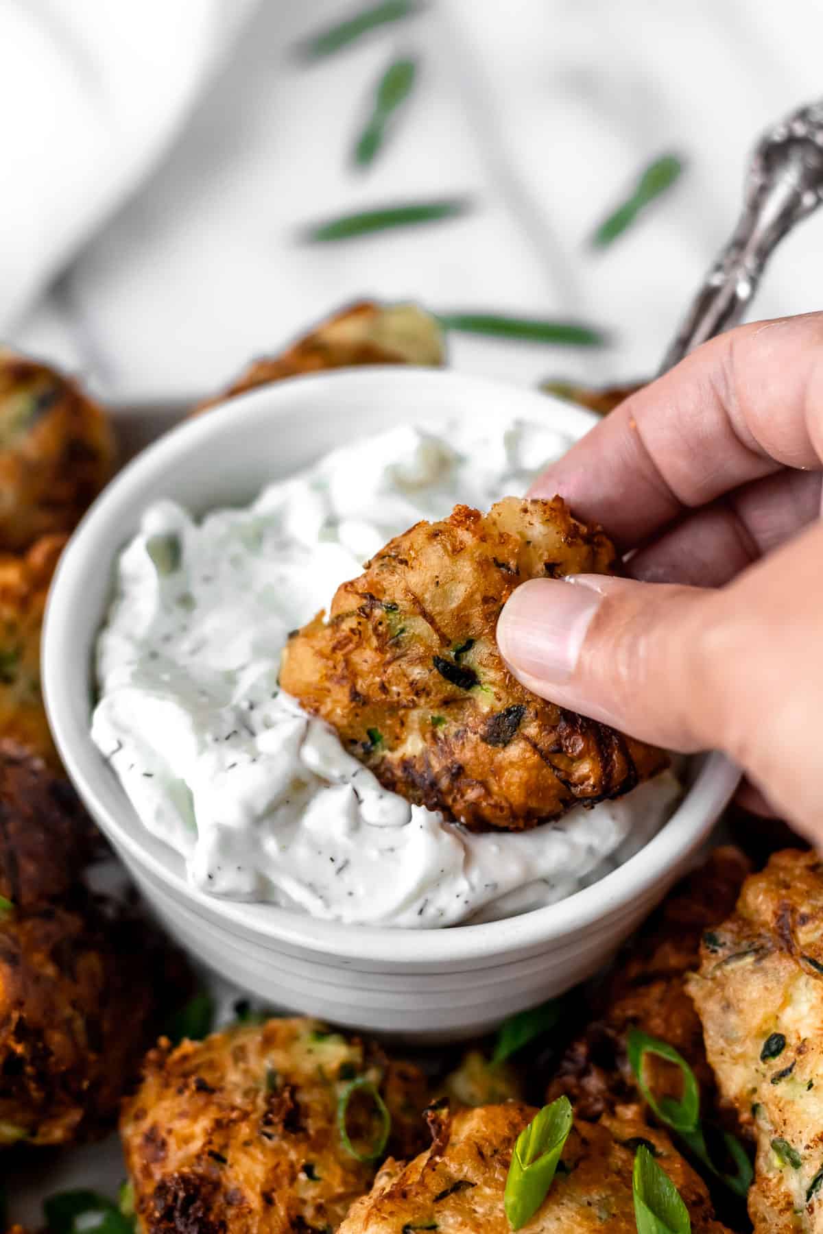 A zucchini fritter being dipped into a bowl of tzatziki sauce.