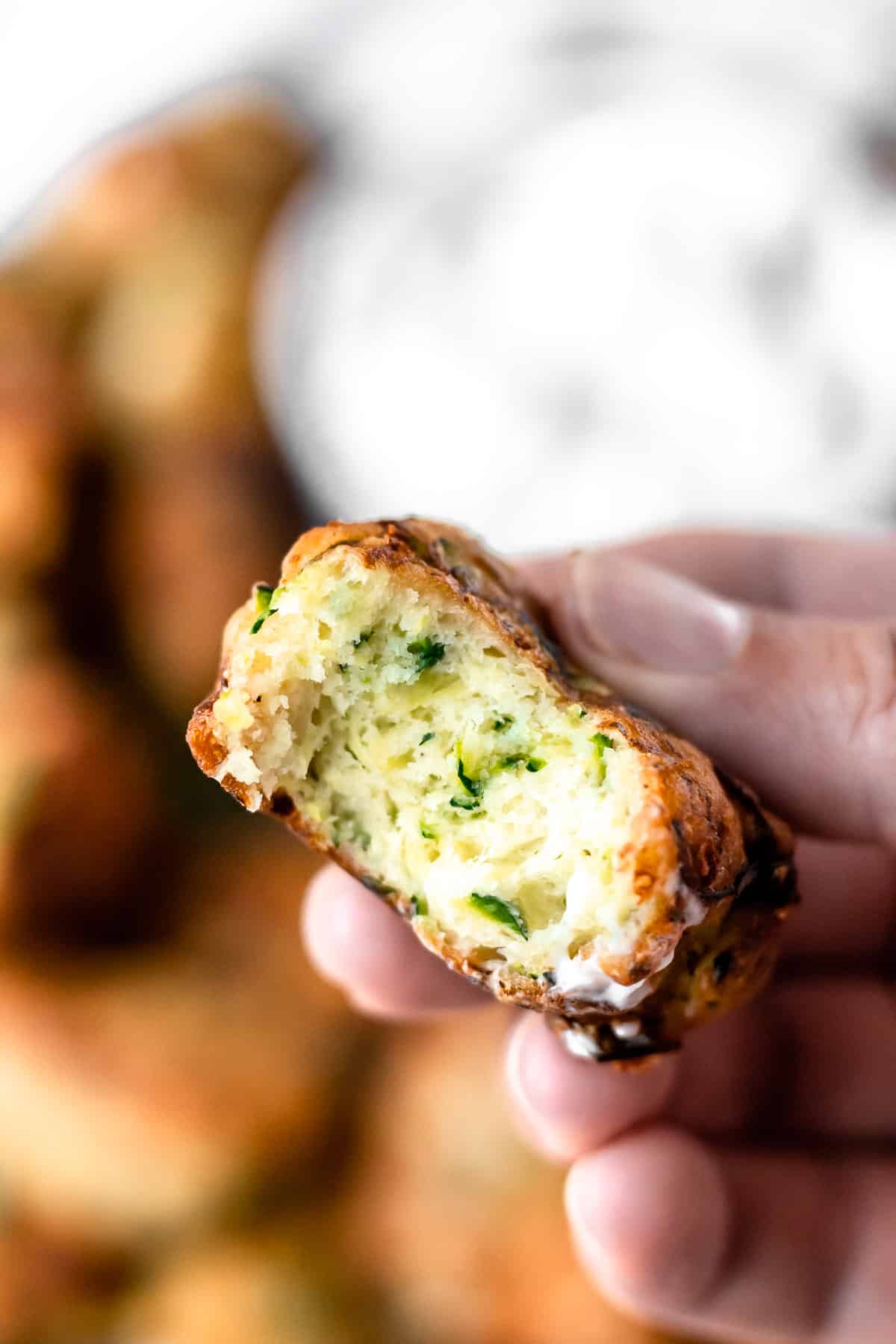 A Greek zucchini fritters with a bite taken out to show the soft, fluffy texture inside of it.