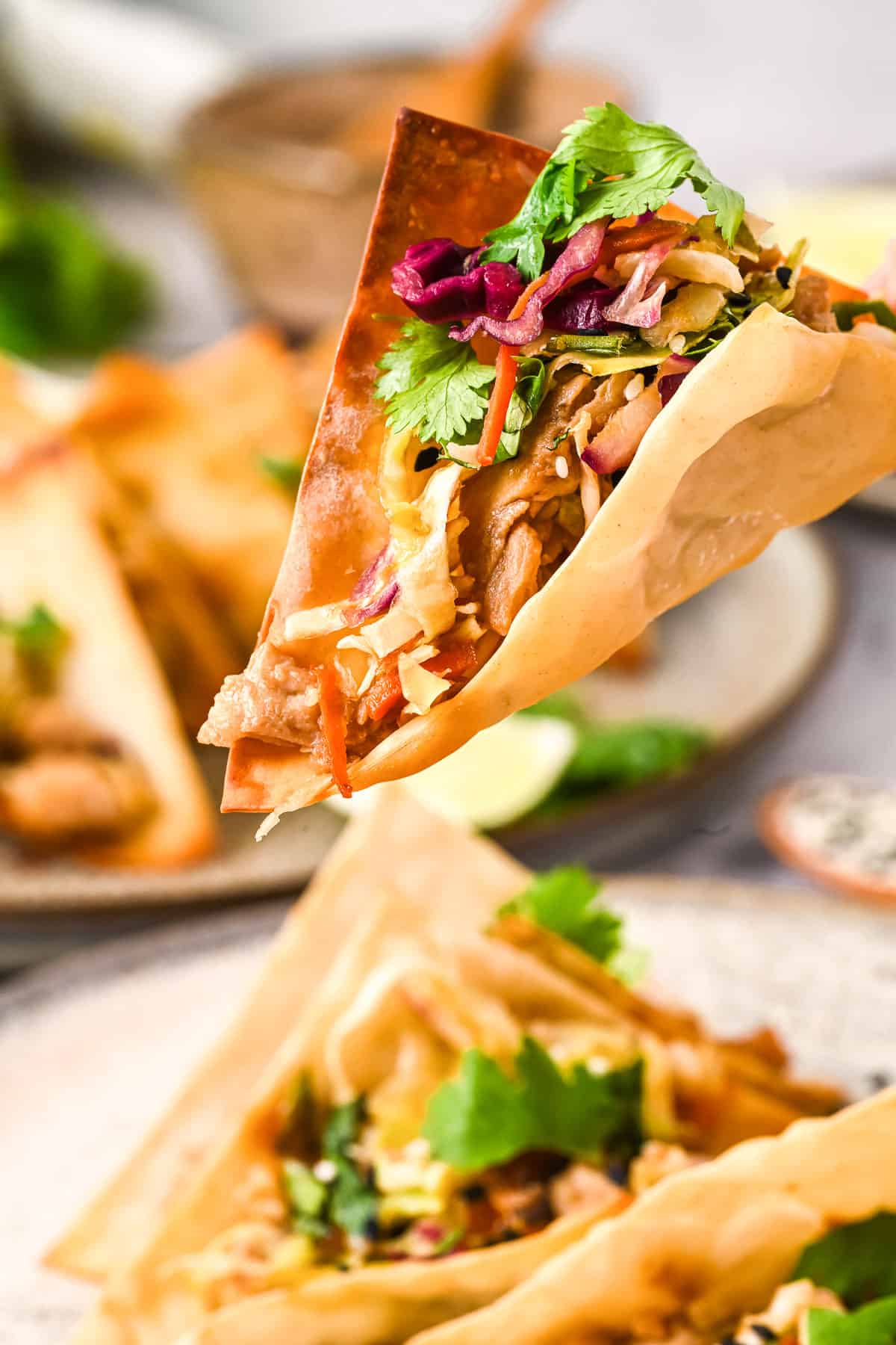 Close up of a wonton chicken taco with a plate of more tacos in the background.