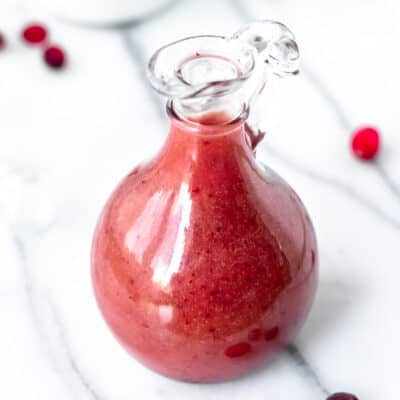 A carafe of cranberry salad dressing with a few cranberries around it.