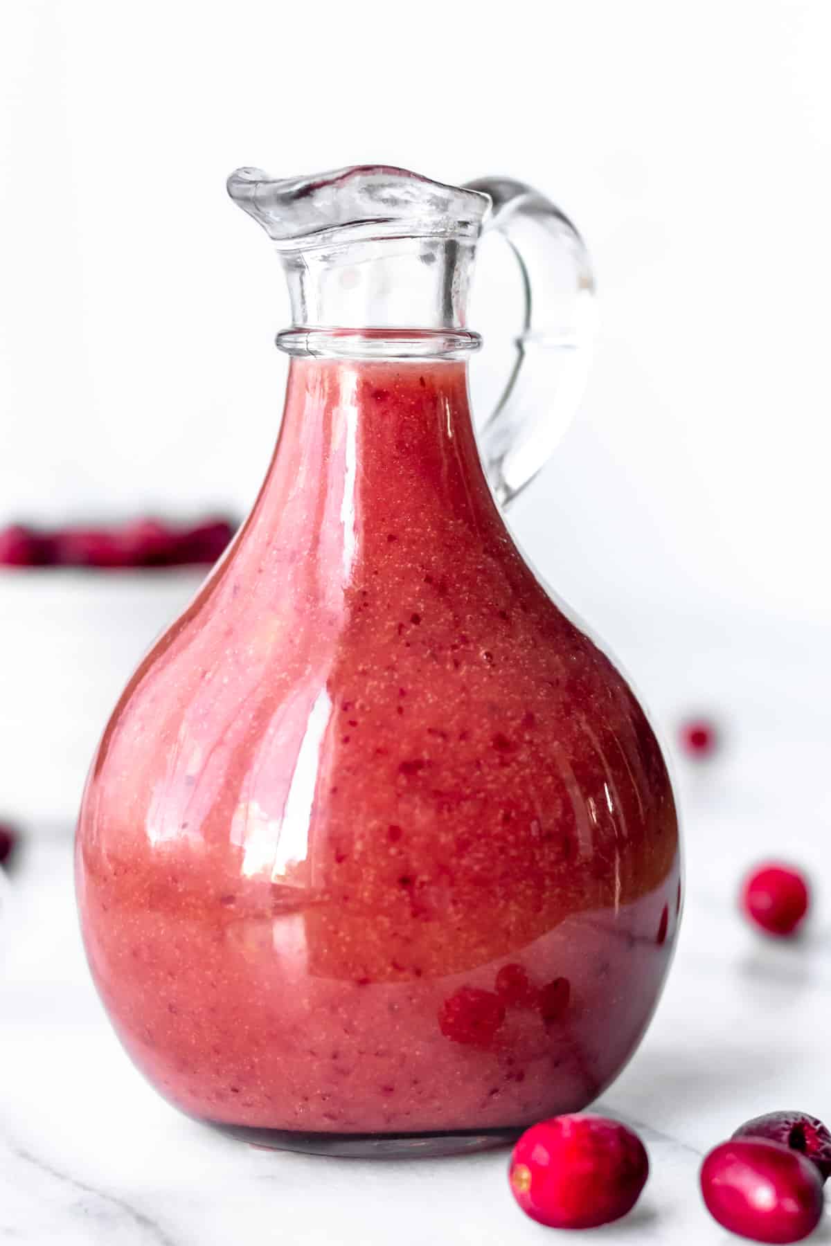 Close up of a carafe of cranberry salad dressing with loose cranberries around it.